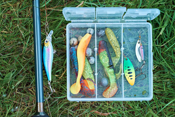 Box with fishing lures on the background of a spinning reel. Fishing gear. View from above