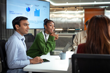 Diverse office business team meeting discussing data visualization with laptop tablet and coffee cup in modern workspace showing collaboration and engagement