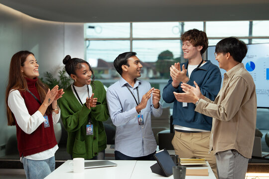 Diverse office business team meeting celebrating success with happy expressions and clapping hands in modern workspace filled with natural light and digital presentation screen