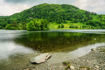 The clear, shallow waters of Rydal Water gently reflect the fresh green slopes of the opposite...