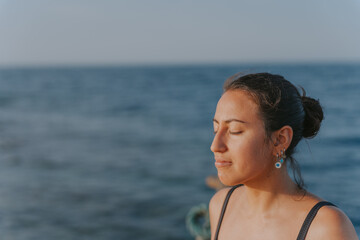 Young woman meditating with closed eyes by the sea at sunset