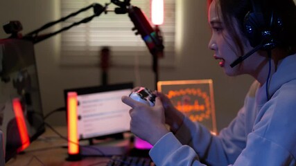 Young Asian female streamer playing video game live stream from home gaming room setup using controller headset Shows focused expression in vibrant lighting - Powered by Adobe
