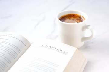 ページを開いたペーパーバック（洋書）とコーヒーの入ったコーヒーカップで、コーヒーを飲みながら読書を楽しんでいるイメージ
