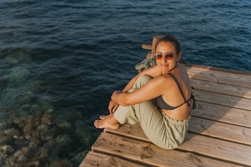 Tourist relaxing on wooden pier by the sea at sunset