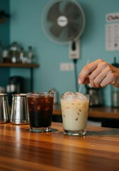 A person's hand places a straw into a cold latte next to an iced coffee on a wooden bar counter. Refreshing drink for hot summer day and heat relief concept.