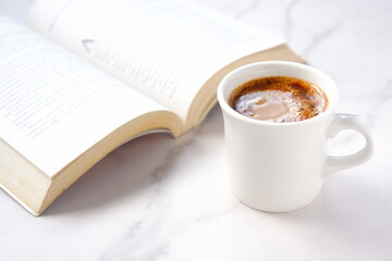 ページを開いたペーパーバック（洋書）とコーヒーの入ったコーヒーカップで、コーヒーを飲みながら読書を楽しんでいるイメージ
