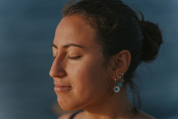Young woman meditating with closed eyes by the sea at sunset