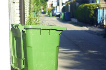 Green garbage container with the lid open on empty residential street in small European town....