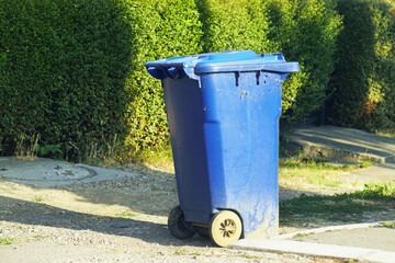 Blue garbage container with lid and wheels on a residential street in summer. Symbolizing of modern recycling and sustainability awareness. Waste management in suburban or small-town neighborhoods