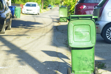 Outdoor green garbage container with open lid against the backdrop of a suburban road and parked...