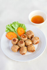 Deep-fried crab rolls wrapped in tofu sheets served with dipping sauce and fresh vegetables. Photographed in natural light to present authentic Thai street food in a homely atmosphere.