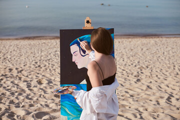 Young female painter stands by sea, absorbed in creating vibrant artwork on canvas. Beach setting...