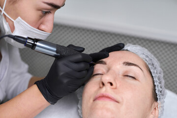 Young woman receives eyebrow permanent makeup in serene spa. Beauty technician, wearing gloves,...