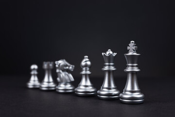 Silver chess piece stand in a row king, queen, bishop, knight, rook, pawn on black background