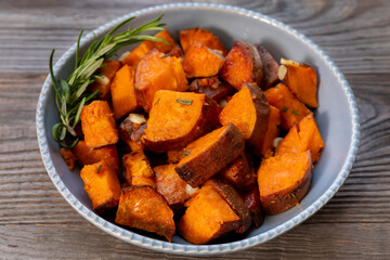 Platter of roasted sweet potatoes decorated with rosemary sprig. Rustic table.