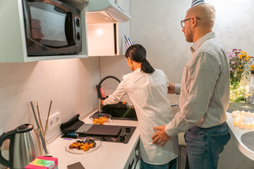 Couple Cooking Kitchen Apartment: Young couple prepares food in modern apartment kitchen; enjoying...