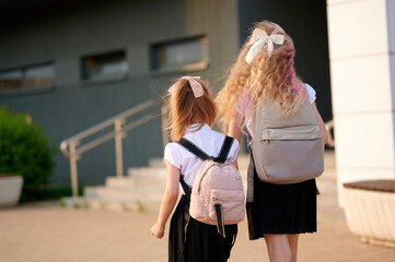 young girls with backpacks walking to school building. sunny day, back-to-school vibes. casual...