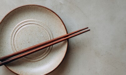 A pair of brown chopsticks resting on a beige plate with a textured surface.