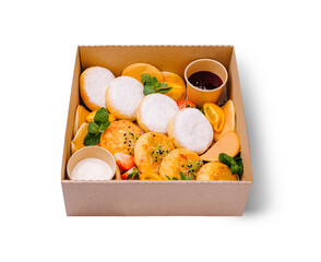 A delightful breakfast box featuring fluffy cottage cheese pancakes dusted with powdered sugar, golden cheese fritters, mini pancakes, fresh fruit slices, and cups of jam and sour cream