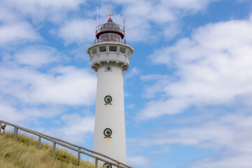 The J.C.J. van Speijk Lighthouse tower with european marram grass (beach grass) under blue sky in summer, Dutch north sea coastline, Egmond aan Zee, Municipality of Bergen, Noord Holland, Netherlands.