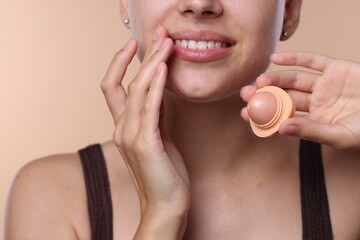 Young woman with lip balm on beige background, closeup