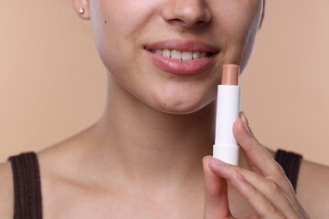 Young woman with lip balm on beige background, closeup