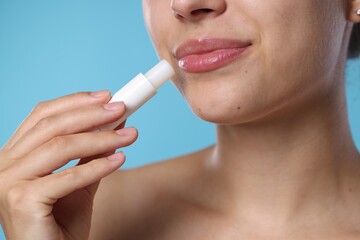 Young woman with lip balm on light blue background, closeup