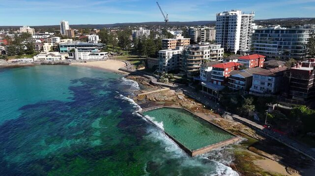 Coastal aerial orbit of Cronulla with oceanfront buildings, waves and clear blue water, Sydney NSW Australia