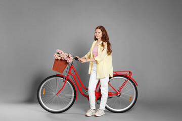 Beautiful teenage girl and bicycle with basket of flowers against grey background