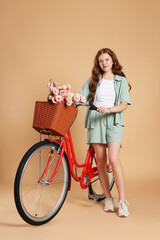 Beautiful teenage girl and bicycle with basket of flowers against beige background
