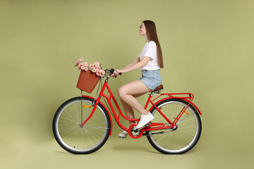 Smiling woman in sunglasses riding bicycle with basket of flowers on green background