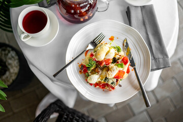 Elegant breakfast with poached eggs, fresh vegetables, and tea served on a white tablecloth in a...