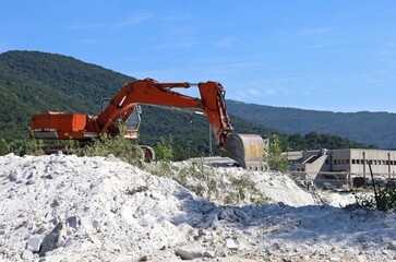 Crawler excavator at work outside a stone processing plant.