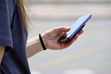 Smartphone in female hand, girl using mobile phone on city street at summer