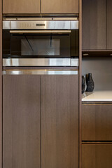 Close-up of a modern stainless steel microwave oven built into dark wood kitchen cabinets. Elegant...
