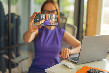 Stylish woman entrepreneur in elegant dress taking selfie at workspace.Modern woman working...