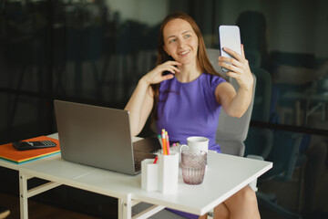 Stylish woman entrepreneur in elegant dress taking selfie at workspace.Modern woman working...