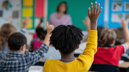 School children raising hands during class with a teacher in front of the blackboard.
