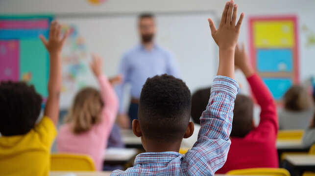 School children raising hands during class with a teacher in front of the blackboard.
