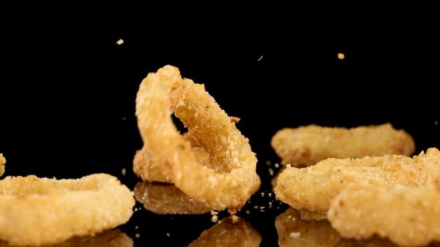 Crispy Fried Onion Rings Dropping Onto Reflective Surface