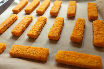Fish fingers in breadcrumbs placed on paper and a baking tray