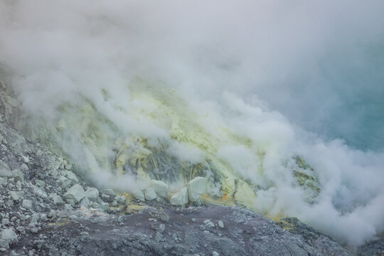 View of sulfurous fumes swirling over the volcanic landscape, with yellow deposits contrasting against the dark rock, Ijen Volcano Crater, East Java, Indonesia.
