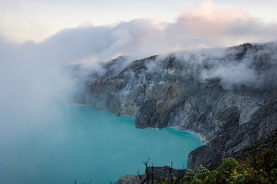View of the turquoise lake nestled within the rugged, volcanic crater, shrouded in ethereal mists and dramatic rock formations, Ijen Volcano Crater, East Java, Indonesia.