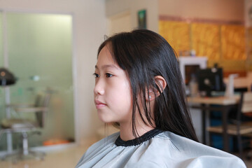 Asian preteen girl having her hair cut. Child sitting in beauty hair salon style for children....