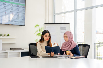 Attractive and cheerful young Asian Muslim businesswoman in hijab enjoy talking with her coworker during the coffee break.