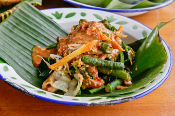 Indonesian vegetable salad with peanut sauce or pecel on vintage enamel plate  lined with banana leaves