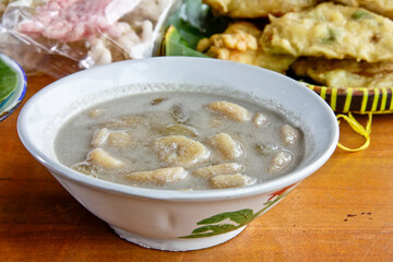 Kolak pisang, traditional Indonesian dessert made of bananas cooked in coconut milk and palm sugar syrup, served  in a white bowl. Setting appears to be a wooden table. 