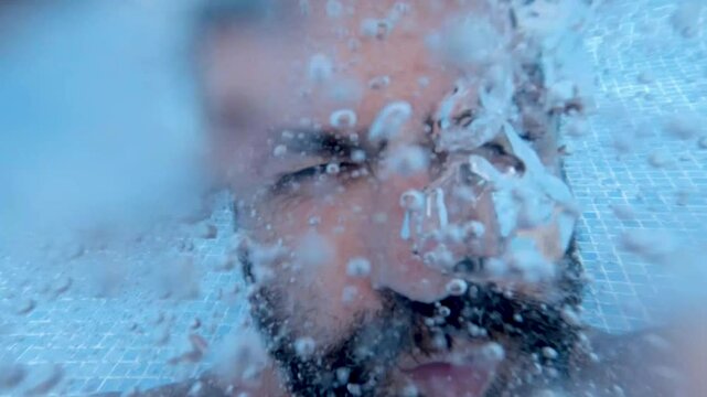 Male swimmer with beard diving underwater, releasing rhythmic bubble stream in swimming pool, depicting underwater submersion with dynamic aquatic movement