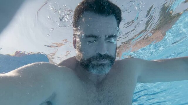 Swimming underwater, bearded male floating serenely, experiencing meditative calm with closed eyes in crystal blue pool depths