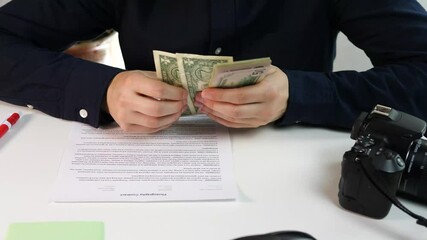 A photographer with a camera and a contract counts the money received for the order. Commercial and professional photography, contract for the creation of photographs